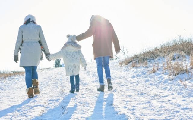 A family dressed in winter gear hiking across a snow-covered field, ideal for showcasing the best winter hiking gear.