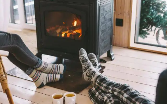 Two people relaxing in front of a fireplace, wearing affordable thermal socks with cozy patterns.