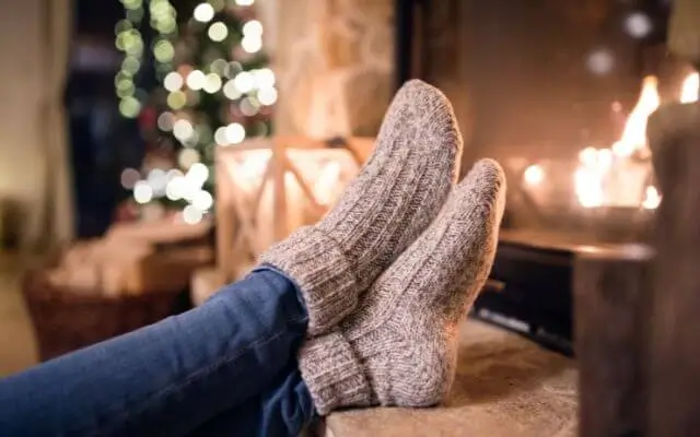 Close-up of a person wearing cozy affordable thermal socks while resting their feet near a warm fireplace.