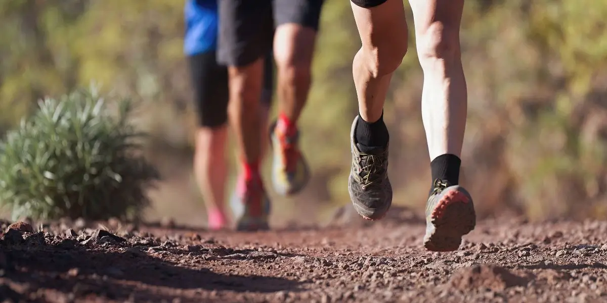 Three runners jogging on a dirt trail, focusing on their legs and trail-running shoes for plantar fasciitis